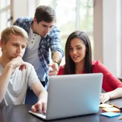 Trzy osoby przy laptopie, jedna wskazuje na ekran.