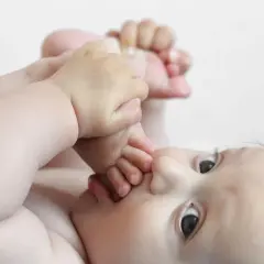 Dziecko leżące na plecach wkłada sobie stopy do buzi.